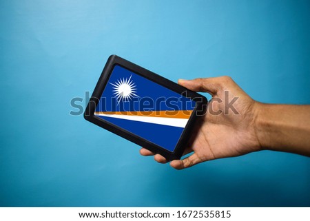 Man holding Smartphone with Flag of Marshall islands. Marshall Islands Flag on Mobile Screen isolated On Blue Background