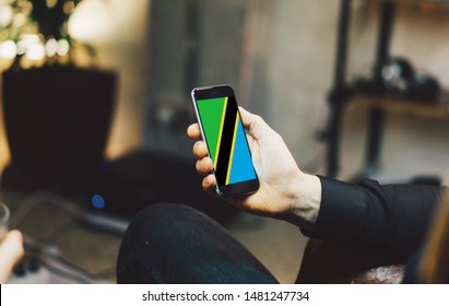 Man Holding Smartphone With Flag Of Tanzania. Tanzania Flag On Mobile Screen.