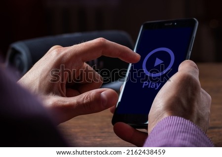 Man holding smartphone and press play button for portable music speaker.