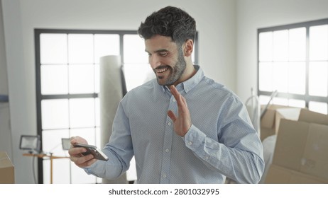 Man holding smartphone and smiling while checking phone among moving boxes in building; contentment progress.
