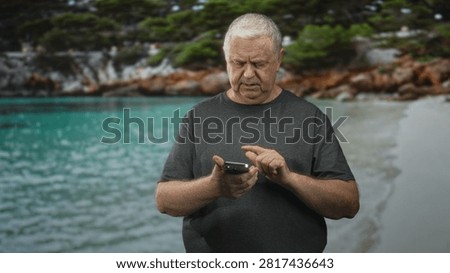 Man holding smartphone, tapping screen with hands in a studio beach setting by turquoise water and rocky shore, looking focused; concentration communication.