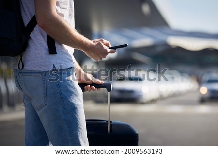 Man holding smartphone and using mobile app against a row of taxi cars. Themes modern technology, carsharing and travel.
