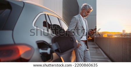 Man holding smartphone while charging car at electric vehicle charging station, closeup.