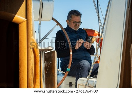 Man holding smartphone while sailing a yacht on the sea
