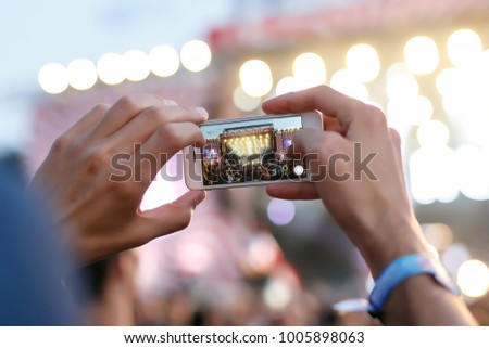 Man holding smartphones in hands and photographing. Taking photo on front stage on summer outdoor music concert festival.