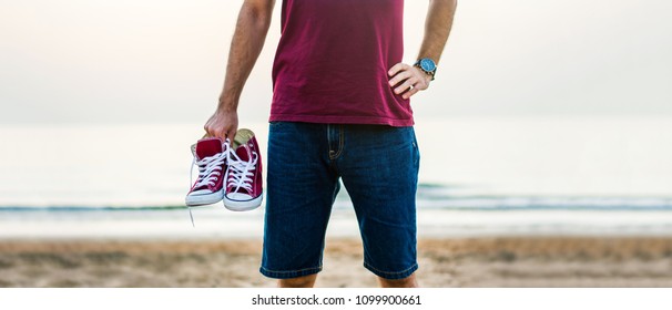 Man Holding Sneakers On The Beach At Dusk