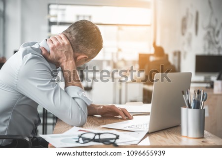Man holding sore neck while using notebook computer. He sitting at table. Sick worker concept