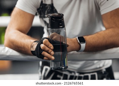 The man is holding a sports bottle with water after hard training. Sportsmen drink water at the gym. The trainer takes a break during session  - Shutterstock ID 2126765561