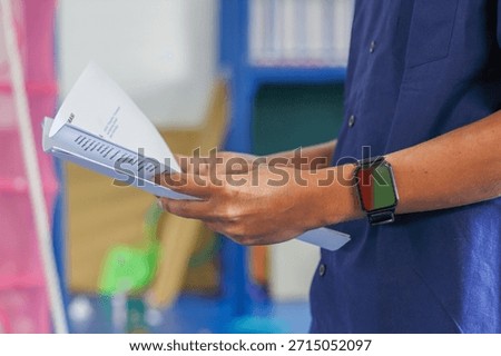 Man Holding a Stack of Paper Documents in a Classroom Setting