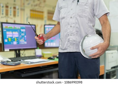 A Man Holding A Staff Safety Helmet With Radio Communication In Production Control Room. There Is A Computer In The Control Of Machinery At Feed Mills. Communication And Safety At Work