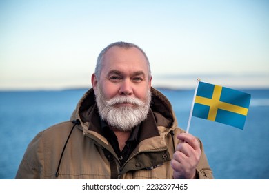 Man holding Sweden flag. Portrait of older man with a national Swedish flag. Visit Sverige Sweden concept. Older man 50 55 60 years old with gray beard outdoors travelling. Travel to Sweden concept. - Shutterstock ID 2232397465