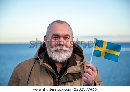 Man holding Sweden flag. Portrait of older man with a national Swedish flag. Visit Sverige Sweden concept. Older man 50 55 60 years old with gray beard outdoors travelling. Travel to Sweden concept.