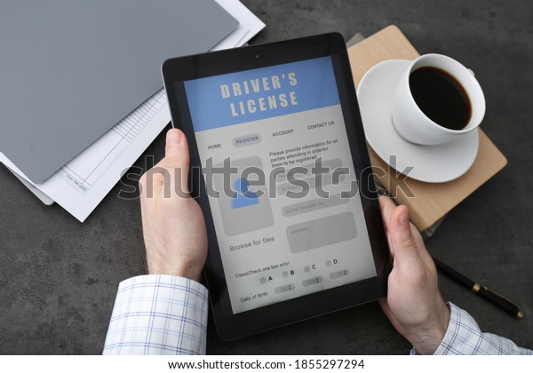 Man holding tablet with driver\'s license\
application form at grey table,\
closeup