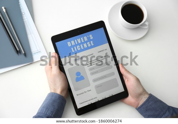 Man holding tablet with driver\'s\
license application form at white table, above\
view