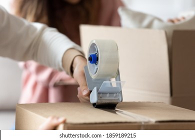 Man holding tape dispenser sealing cardboard box with personal stuff belongings on happy moving day to own house. Family prepare parcel, send cheap services ad, relocation to new apartment concept - Shutterstock ID 1859189215