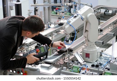 Man is holding teach panel to control a robotic arm which is integrated on smart factory production line. industry 4.0 automation line which is equipped with sensors and robotic arm. Selective Focus.