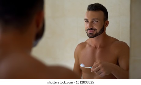 Man Holding Toothbrush With Toothpaste Looking In Mirror At Bathroom, Dentalcare