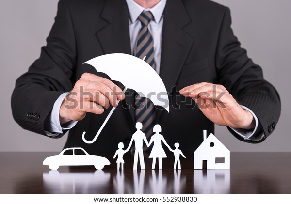 Man holding an umbrella protecting a family, a house\
and a car