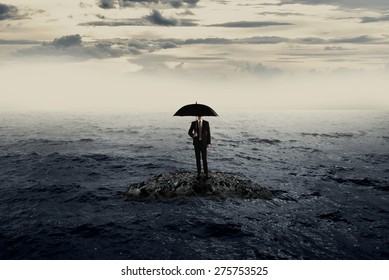 Man holding umbrella standing on the rock on the sea with bad weather. Business recession concept