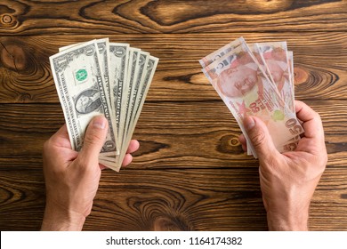 Man Holding USD And Turkish Lira In His Hands Over A Wooden Table Viewed From Above In A Concept Of Monetary Crisis, Devaluation, Foreign Exchange, Emerging Markets And Currencies