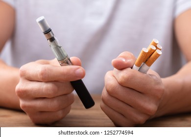 Человек, держащий вейп и табачную сигарету над столом