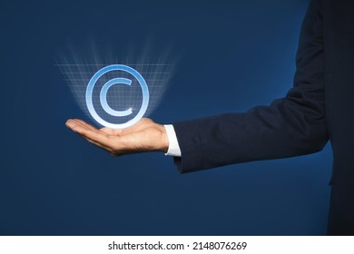 Man Holding Virtual Icon Of Copyright Symbol On Blue Background, Closeup