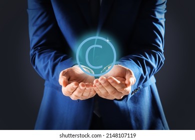 Man Holding Virtual Icon Of Copyright Symbol On Dark Background, Closeup