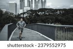 A man holding a water bottle, smartphone and listen music earphone while  running up on footbridge in the city center park for cardio workout.  Health and Lifestyle in big city life concept.