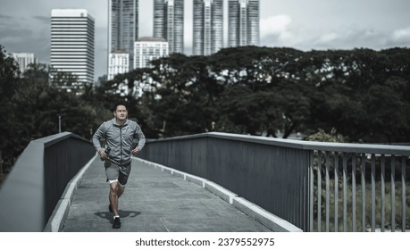 A man holding a water bottle, smartphone and listen music earphone while  running up on footbridge in the city center park for cardio workout.  Health and Lifestyle in big city life concept. - Powered by Shutterstock