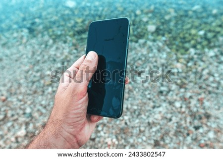 Man holding wet waterproof mobile phone found in sea water, selective focus