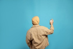 Man Holding White Can Of Spray Paint On Light Blue Background, Back View