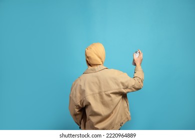 Man holding white can of spray paint on light blue background, back view