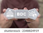 Man holding white plastic foam blocks with icons and abbreviation: BDC. Concept of BDC Business Development Company.