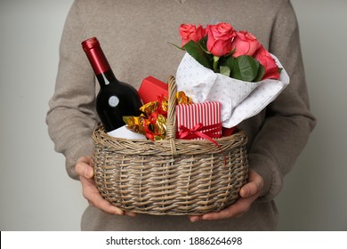 Man holding wicker basket with gifts, bouquet and wine on grey background, closeup - Powered by Shutterstock