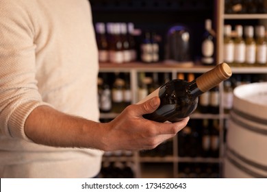 A man holding  a wine bottle in a liquor wine shop. Choosing the right wine from all the variations of wine bottles on the shelves in the bokeh background. - Powered by Shutterstock