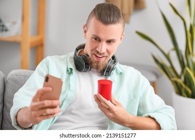 Man Holding Wireless Portable Speaker And Mobile Phone On Sofa