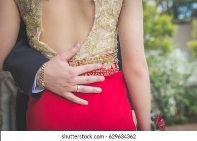 Man Holding Woman Around Waist With His Hand On Woman's Lower Back Dressed In Formal Wear