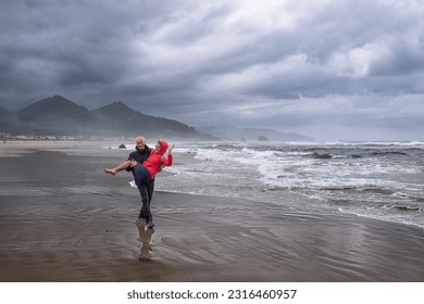 Man holding woman in his hands on the  beach. Middle age people having fun. Cannon beach. Portland. Oregon. USA