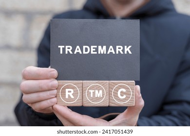 Man holding wooden cubes with icons and black sticky note with word: TRADEMARK. Trademark TM Business Brand Copyright Patent Concept.