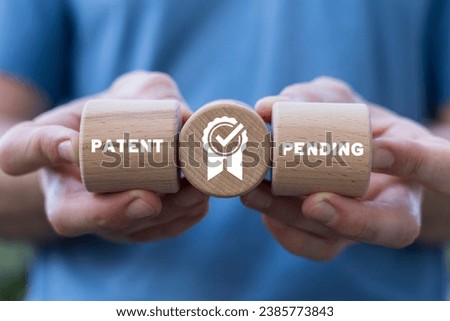 Man holding wooden cylinders sees inscription: PATENT PENDING. Concept of patent pending. Patented product. Registered intellectual property, patent license certificate submission.
