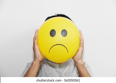 A man holding a yellow balloon with sad face emotion instead of head - Powered by Shutterstock