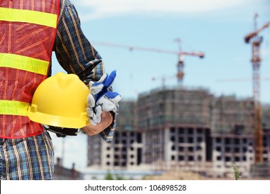 man holding yellow helmet in front of construction site