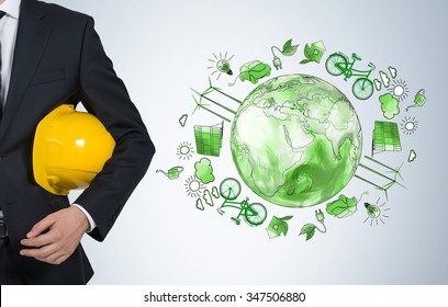 Man Holding A Yellow Helmet, A Green Picture Of Eco Energy Icons Arranged In Circle, Earth In The Centre To The Right Of Him, Concept Of Clean And Safe  Environment, Breast View