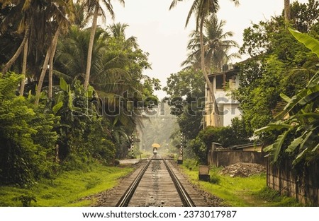man holding a yellow umbrella crossing a train rail surrounded by coconut palms in Sri Lanka