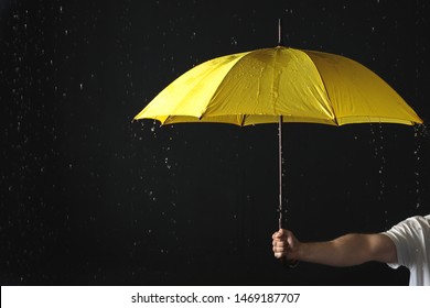 Man holding yellow umbrella under rain against black background, closeup - Powered by Shutterstock