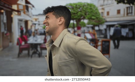 Man holds back while he leans against street sign beside hispanic young guy near cafe, trying to mask pain and discomfort.