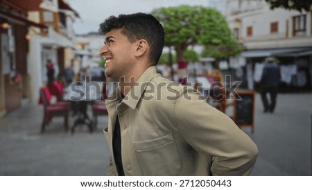 Man holds back while he leans against street sign beside hispanic young guy near cafe, trying to mask pain and discomfort.