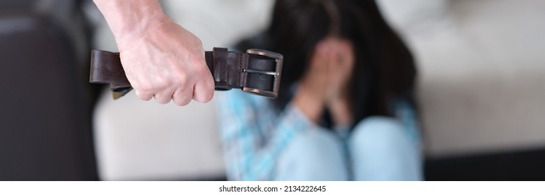 Man Holds Belt In Fist Against Background Of Crying Woman Closeup