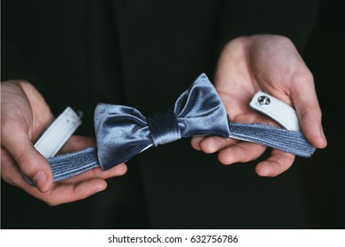 A Man Holds A Blue Velvet Bow Tie In His Hand On A Black Background