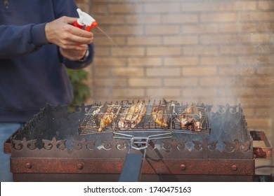 Man Holds A Bottle Of Spray With Water In His Hands And Pours A Mackerel Fish Roasting On The Grill
